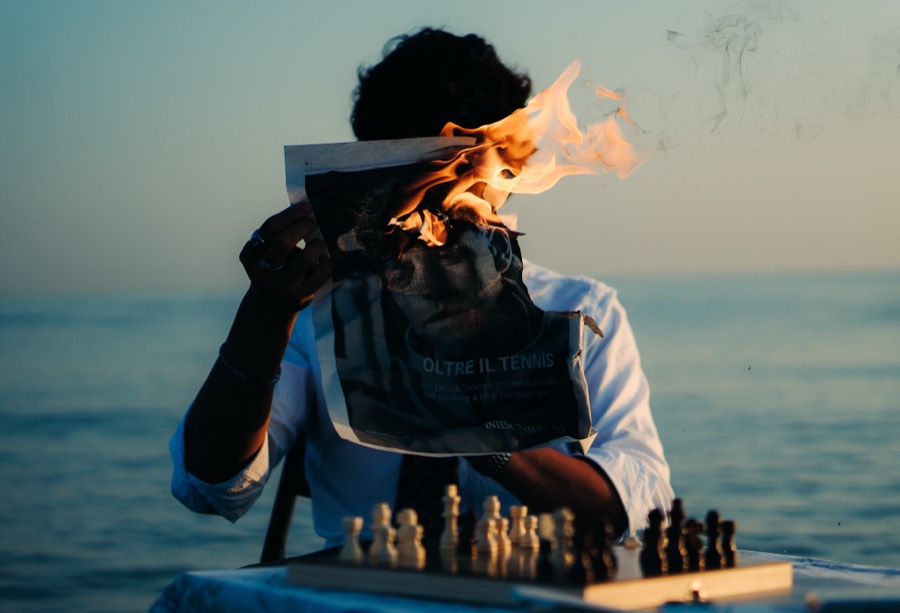 MAN AT SEA — CHESS &mdash; A surreal beach concept: chess, fire, and a burning newspaper at sea.